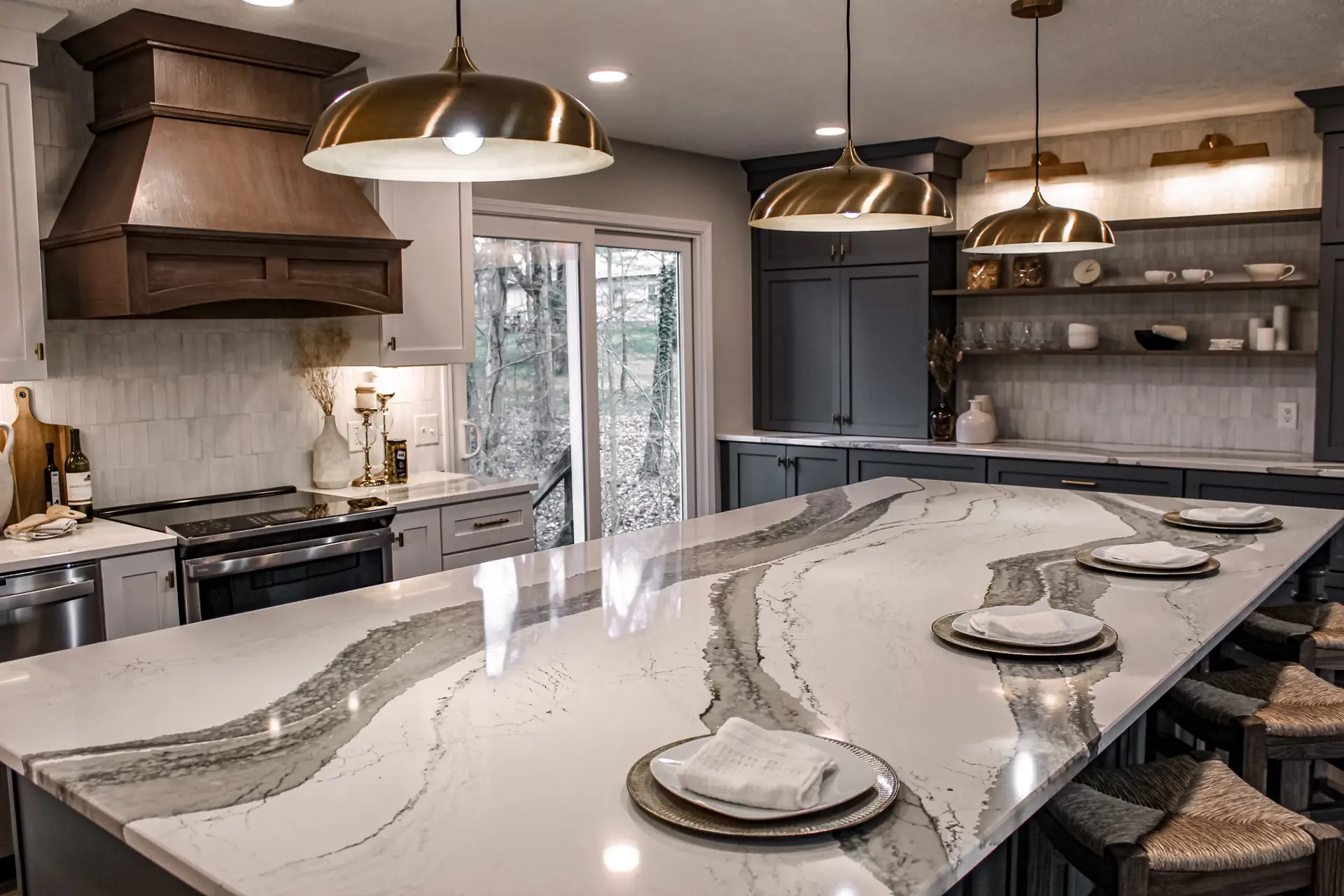 Modern kitchen with a large marble island, gray cabinets, and brass pendant lights over the counter