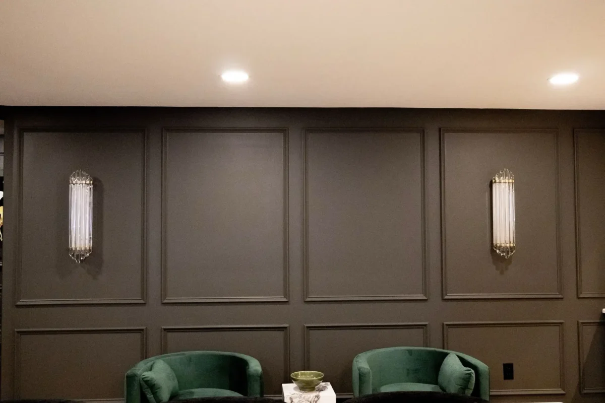Dark paneled wall with two crystal wall sconces and a teal seating area in a cozy lounge.