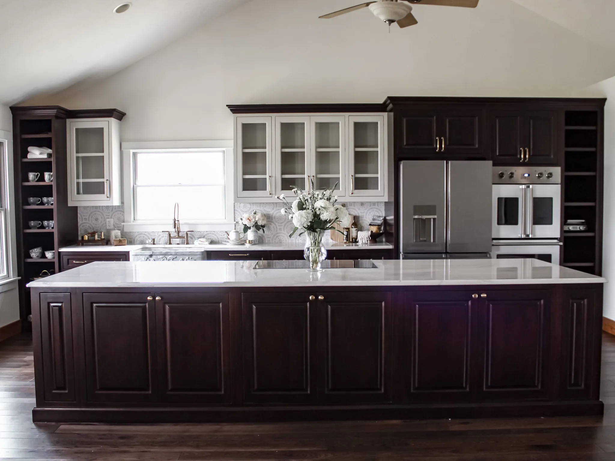 Kitchen addition with a vaulted ceiling, a long dark wood island with a white countertop, glass-front cabinets, and a stainless refrigerator and wall ovens